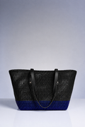 A black woven tote bag with a blue gradient bottom and black shoulder straps, photographed against a neutral gray studio background.