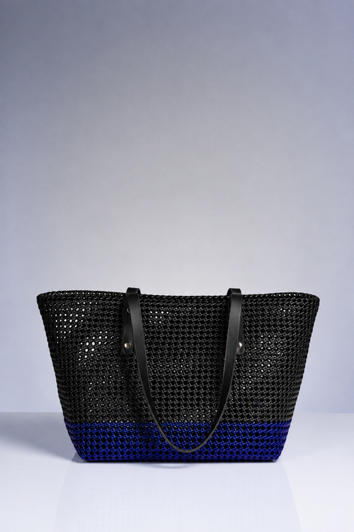 A black woven tote bag with a blue gradient bottom and black shoulder straps, photographed against a neutral gray studio background.