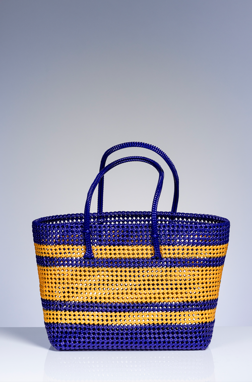 A woven basket bag with horizontal stripes in royal blue and golden yellow, featuring two top handles, set against a neutral gray studio background.
