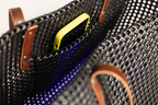 Close-up of a black woven basket bag with brown leather handles and a yellow phone partially tucked into a side pocket.