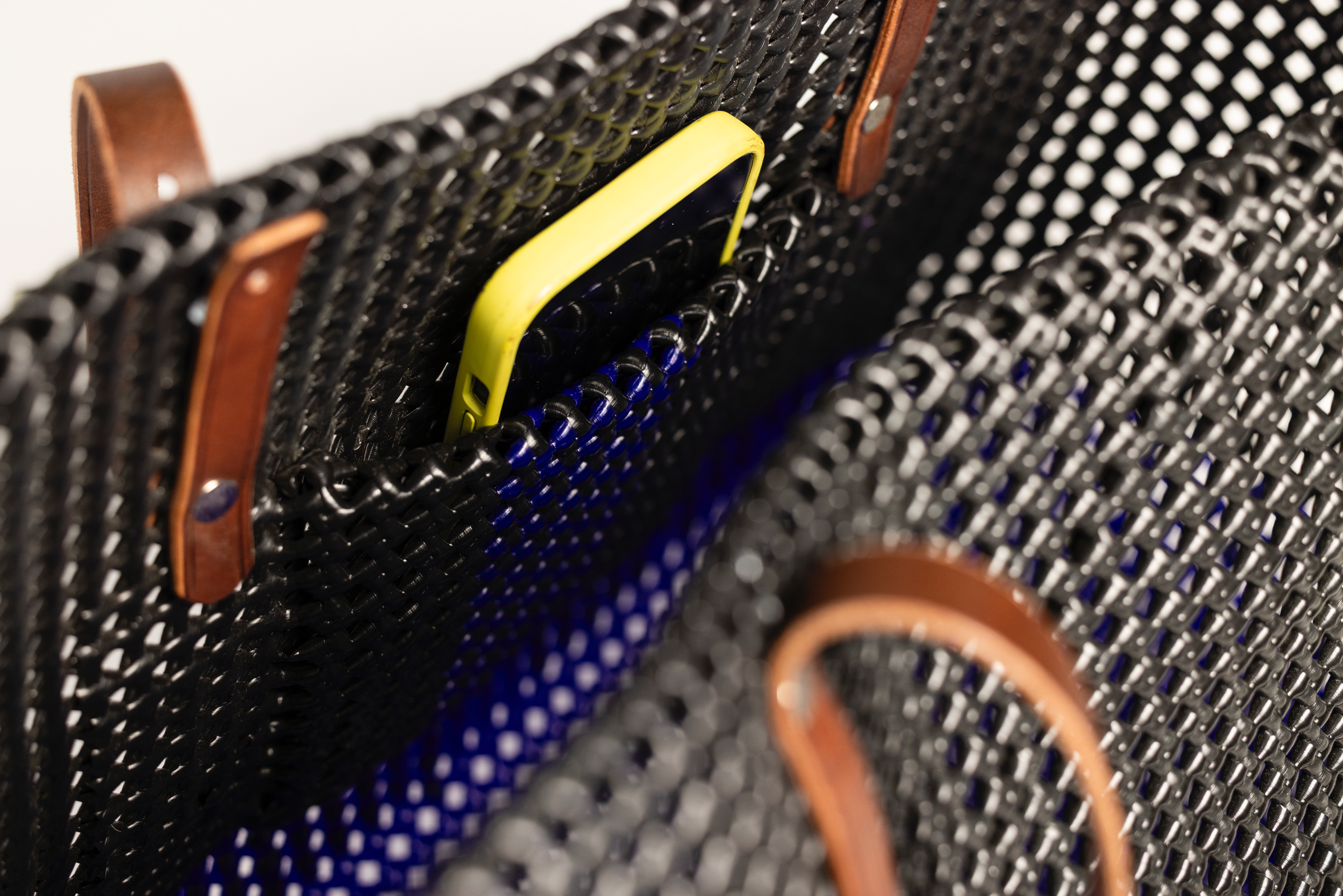 Close-up of a black woven basket bag with brown leather handles and a yellow phone partially tucked into a side pocket.