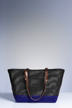 A woven basket bag with a black mesh upper body, a vibrant blue bottom base, and brown leather shoulder straps, set against a neutral gray studio background.