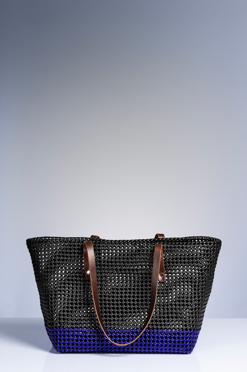 A woven basket bag with a black mesh upper body, a vibrant blue bottom base, and brown leather shoulder straps, set against a neutral gray studio background.