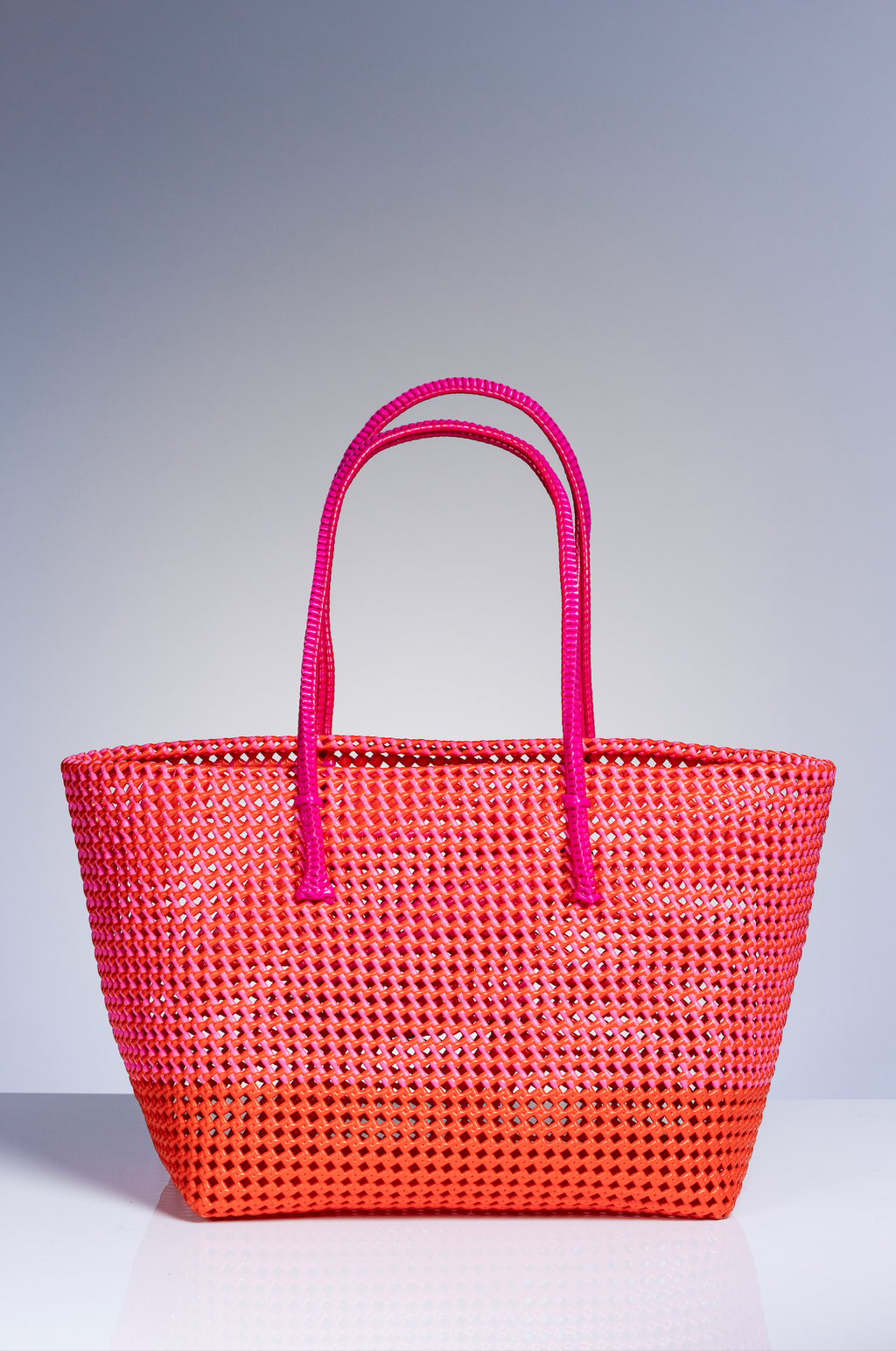 A bright orange woven tote bag with magenta-pink double shoulder straps, shown on a neutral gray gradient background.