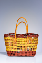A woven tote bag with horizontal stripes in yellow, brown, and dark reddish-brown, featuring two tan shoulder straps, set against a gradient gray studio background.