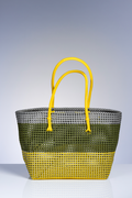 A woven straw tote bag with a three-tone color-blocked design in olive green, gray, and bright yellow, featuring matching yellow handles, set against a gradient gray studio background.